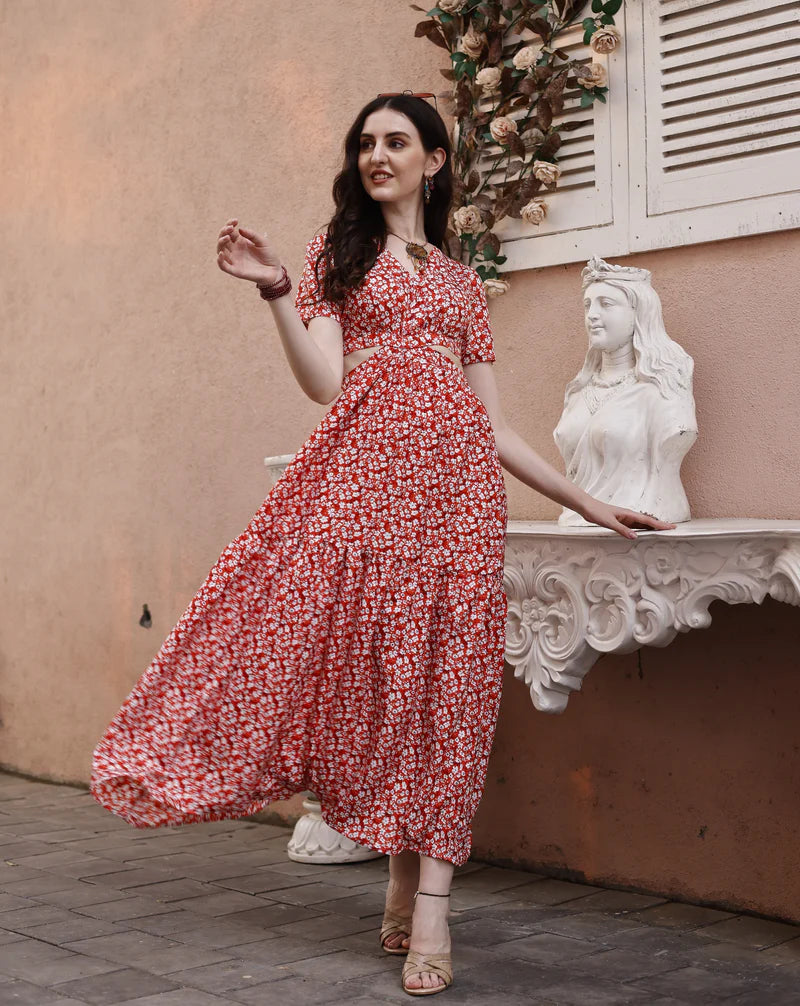 Woman in a red floral maxi dress posing outdoors near a white decorative statue and wall.