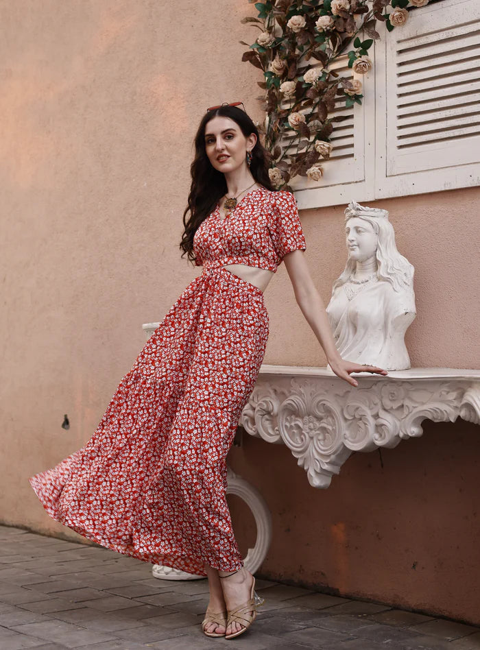 Woman in a red floral cut-out maxi dress posing outdoors by a decorative wall and statue