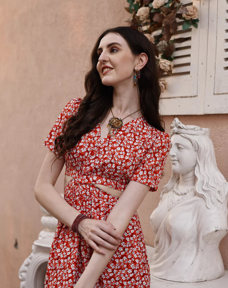 Woman in red floral dress with cutout, standing beside a white statue and vintage decor.