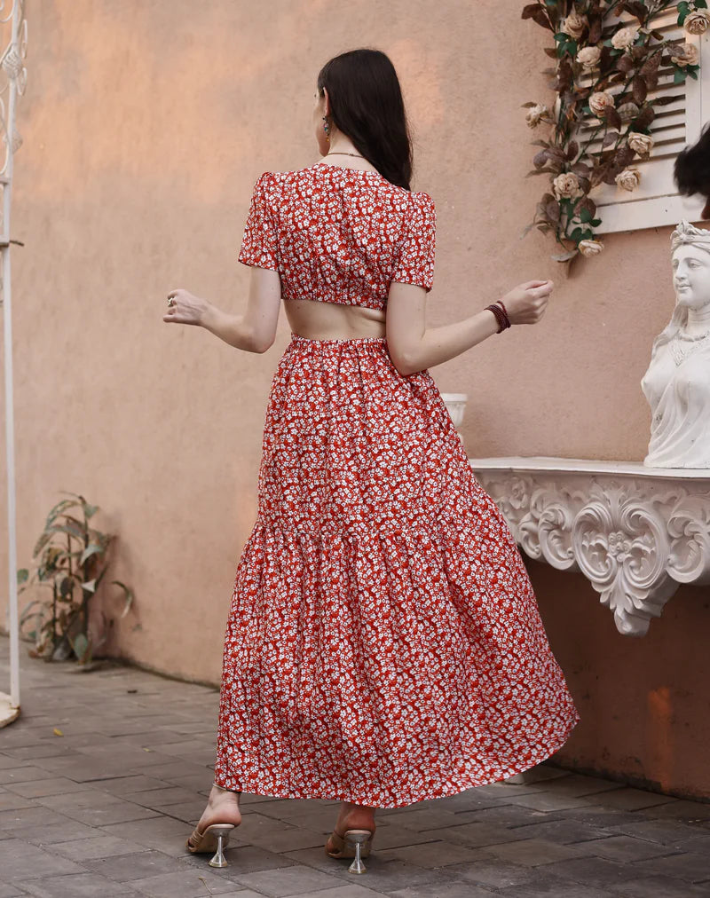 Woman in red floral maxi dress with open back, standing outdoors by peach wall and white decor