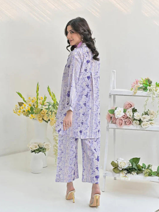 Woman in lavender floral print pajama set with long sleeves, standing near flowers