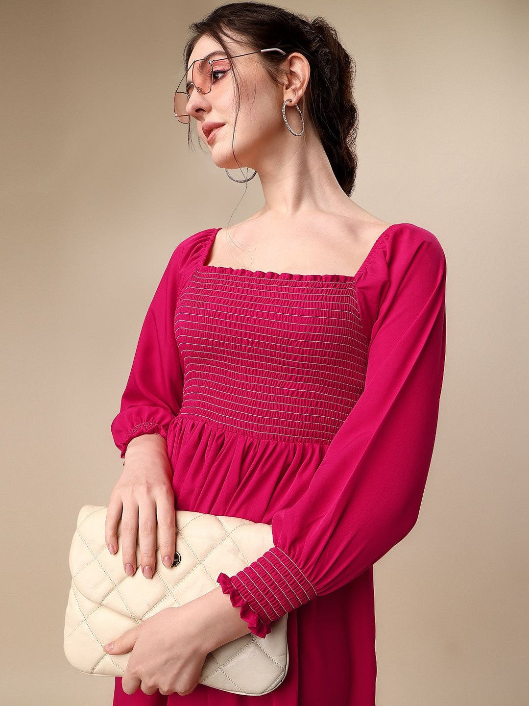 Woman in a pink smocked dress holding a quilted cream clutch against beige background