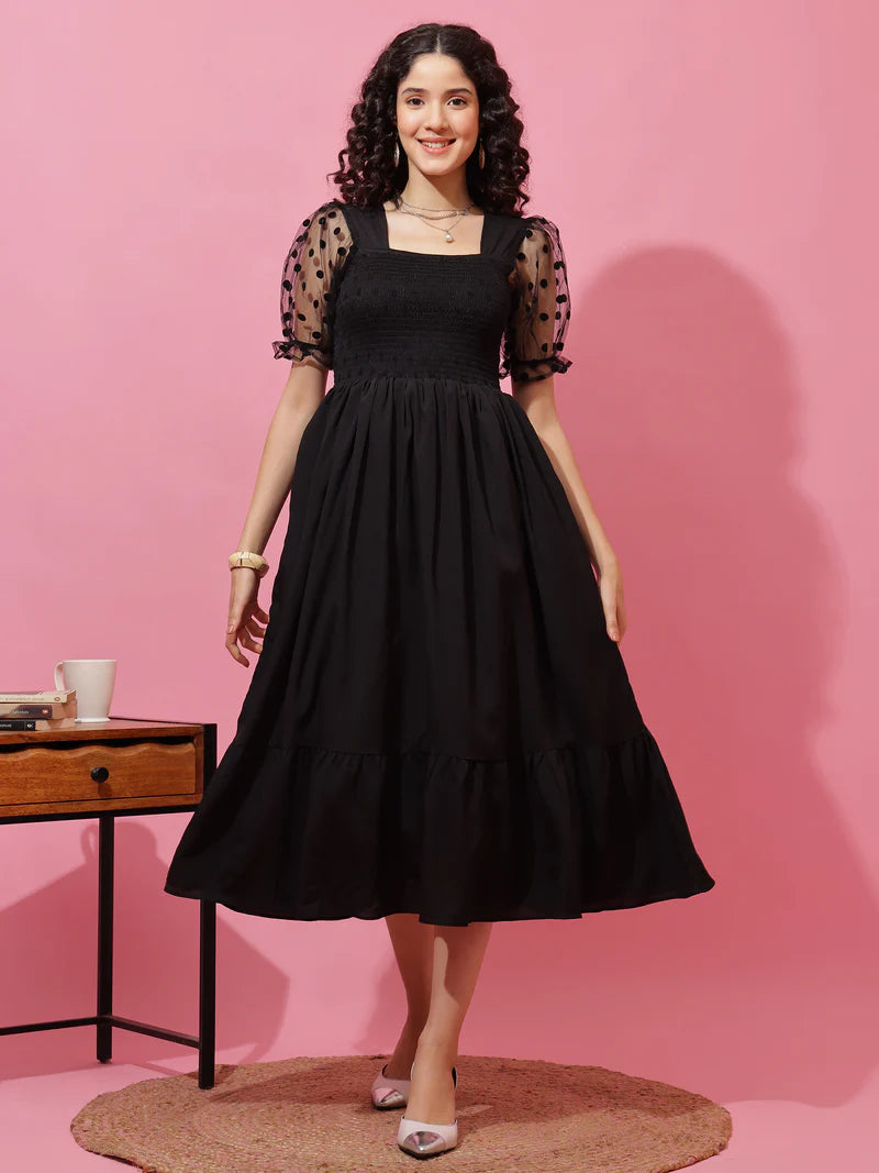 Woman wearing black midi dress with sheer polka dot puff sleeves, standing against pink background