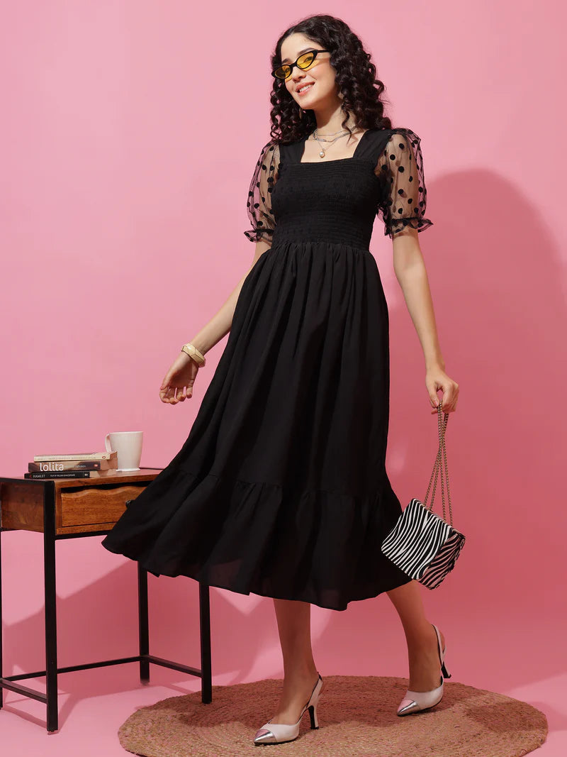 Woman in a black midi dress with sheer polka dot sleeves, holding a striped bag, pink background