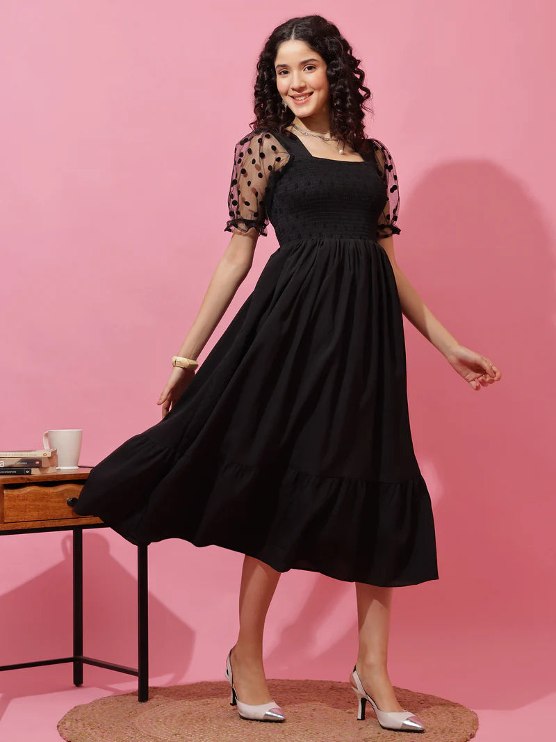 Woman wearing black midi dress with sheer polka dot puff sleeves, posing against pink background