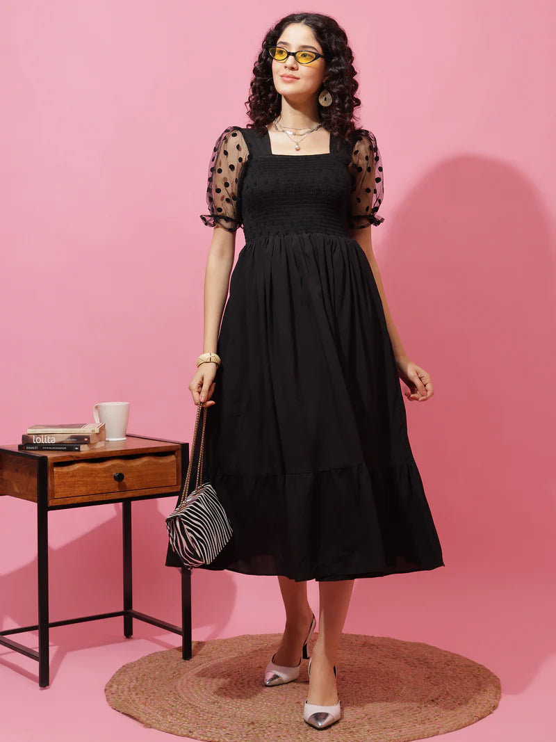 Woman in black midi dress with sheer polka dot sleeves, holding striped handbag