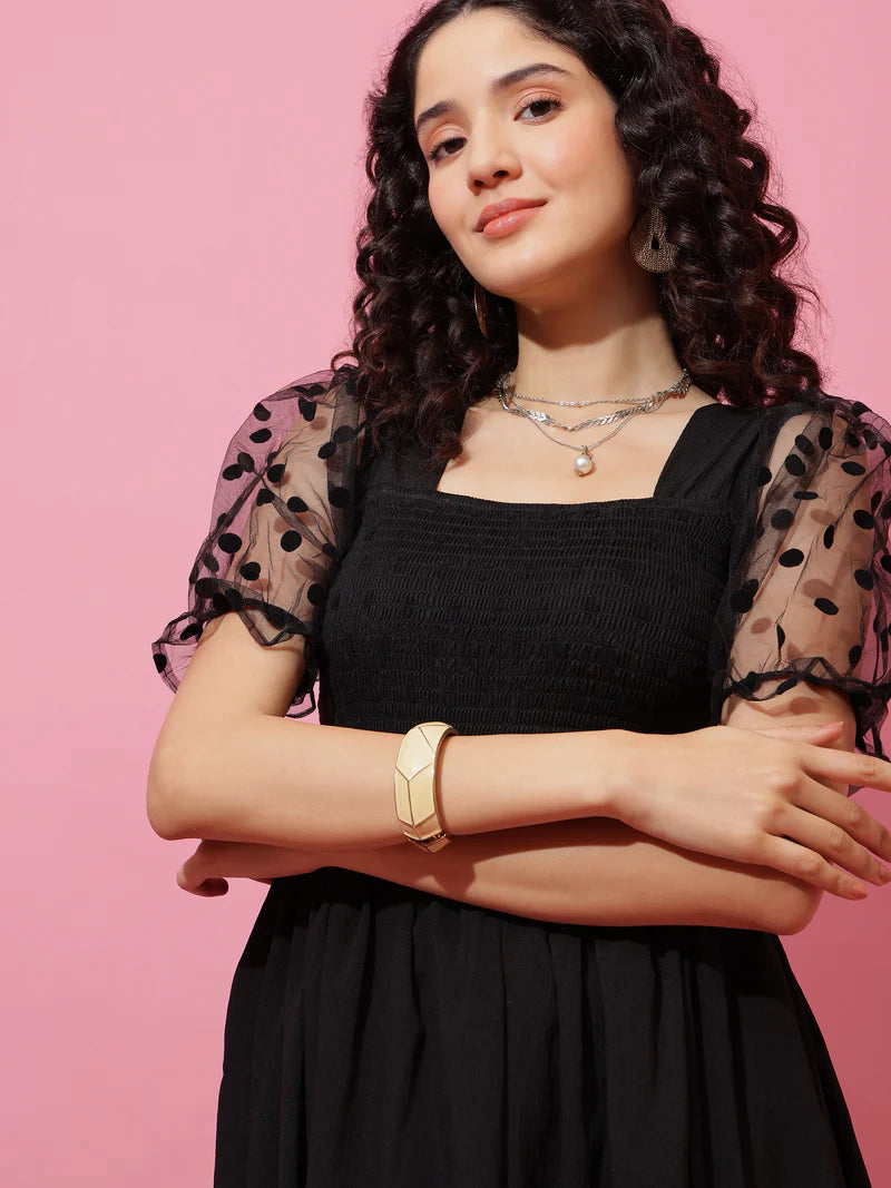 Woman in black dress with mesh polka dot puff sleeves, layered necklaces, and gold bracelet