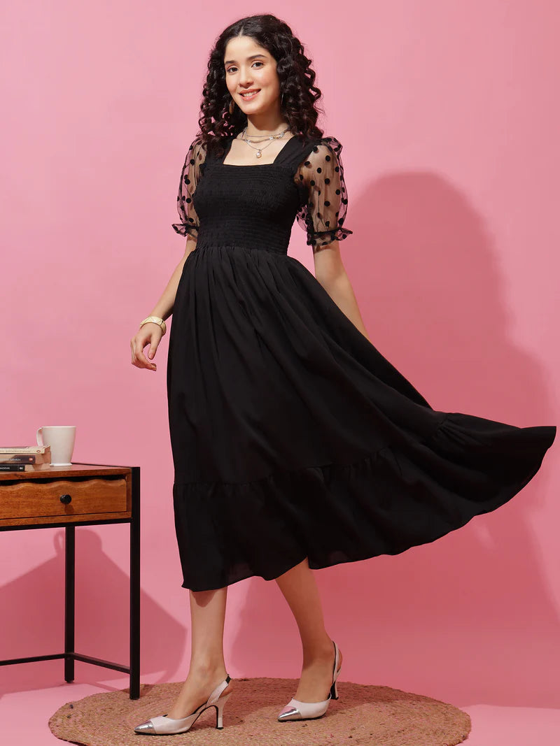 Woman in black midi dress with sheer polka dot sleeves, posing against pink background