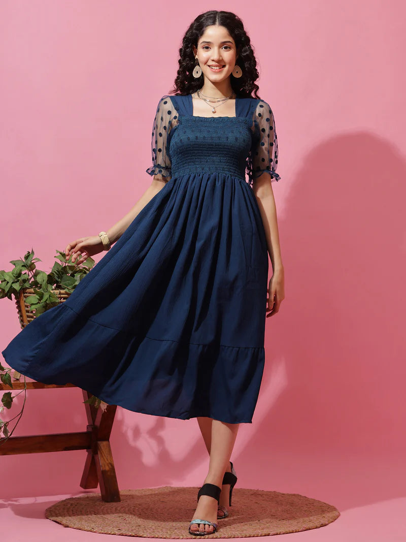 Woman in navy blue smocked midi dress with sheer polka dot sleeves, pink background