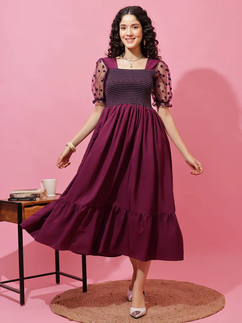 Woman in a purple midi dress with sheer polka-dot puff sleeves, standing on a rug