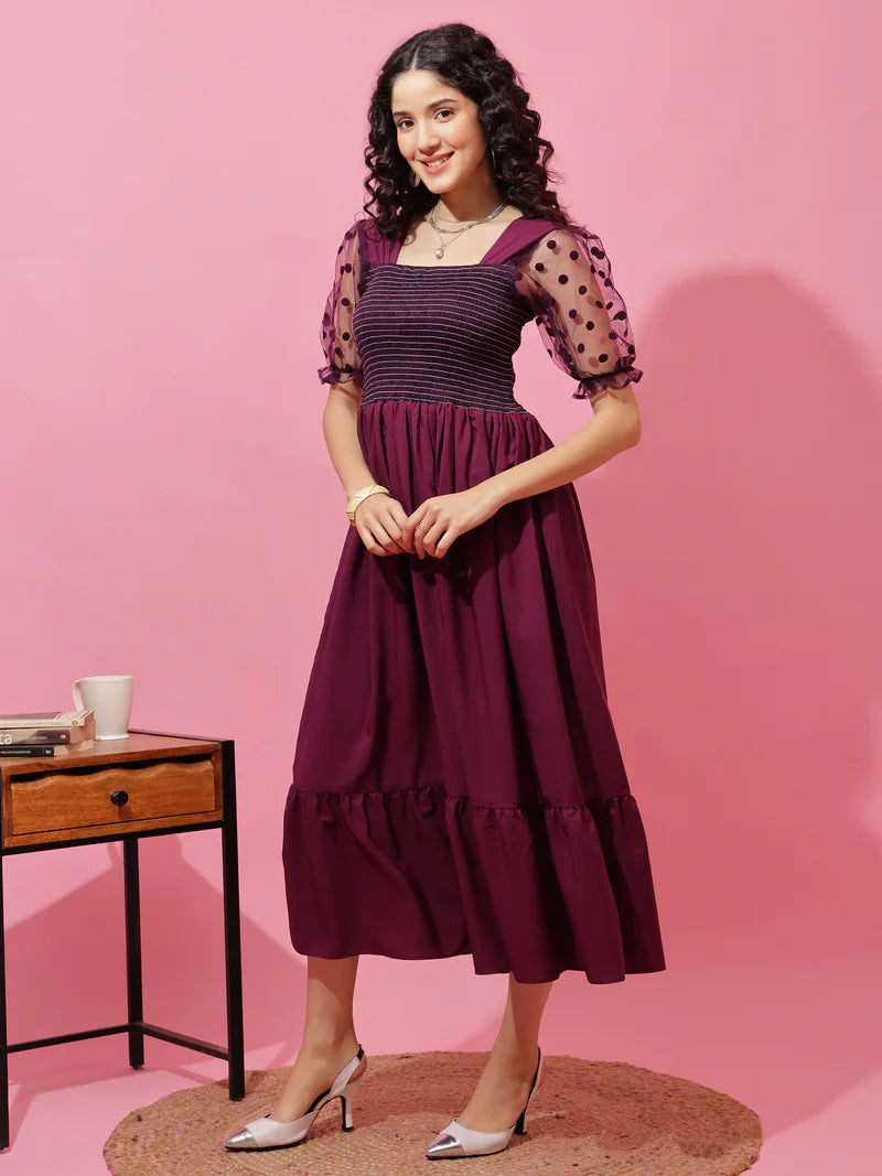 Woman wearing a purple midi dress with puffed sheer polka dot sleeves, pink background